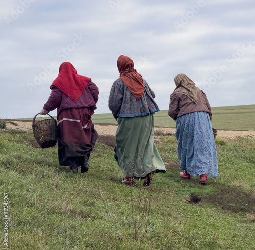 Three women are walking in a field, one of them carrying a basket photo