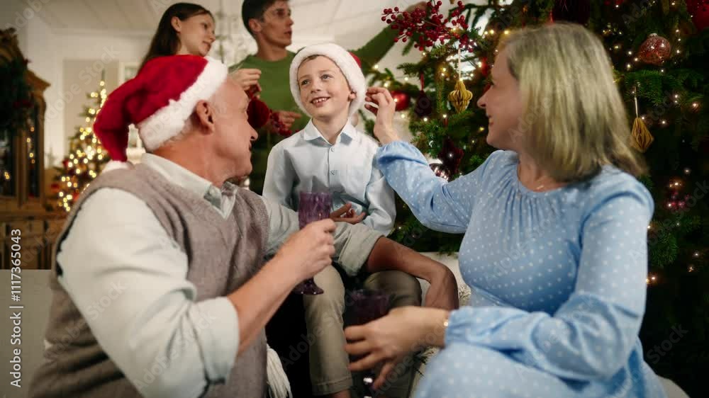 Warm family atmosphere in Christmas vacation, portrait of boy and grandparents. Cheerful little child and senior man and woman sitting on sofa in living room, parents decorating Xmas tree, happiness Warm family atmosphere in Christmas vacation, portrait of boy and grandparents. Cheerful little child and senior man and woman sitting on sofa in living room, parents decorating Xmas tree, happiness