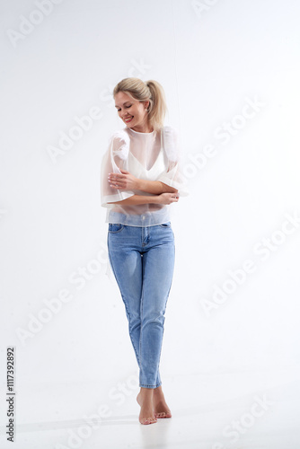 Blonde in a white T-shirt and blue jeans poses in a studio on a white background.