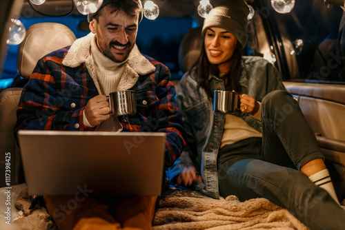 Cozy couple in a car trunk talking and sipping hot beverages on a chilly evening