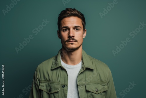 A man with a beard and a green jacket is standing in front of a green wall