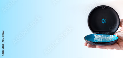 Banner, hand holding Invisalign transparent braces on blue background with copy space. Orthodontic invisible retainers and aligners