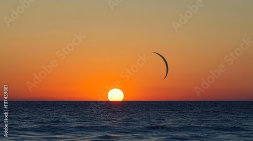 Silhouette of kitesurfer at sunset over ocean.