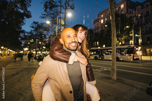 Fotografie A smiling couple delight in a piggyback ride along a lively city street at night enhancing the romantic evening ambiance