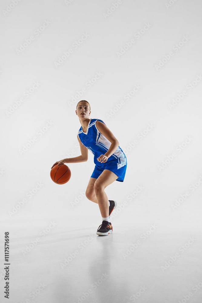 Dribbling. Full-length image of young concentrated teen girl in blue uniform, playing basketball, training against white studio background. Concept of sport, youth, motion, healthy lifestyle Dribbling. Full-length image of young concentrated teen girl in blue uniform, playing basketball, training against white studio background. Concept of sport, youth, motion, healthy lifestyle