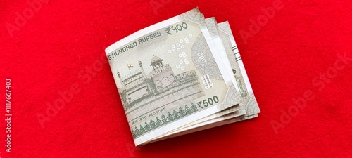 Fotografija A bundle of folded five hundred Indian rupee bank paper currency notes on red table background
