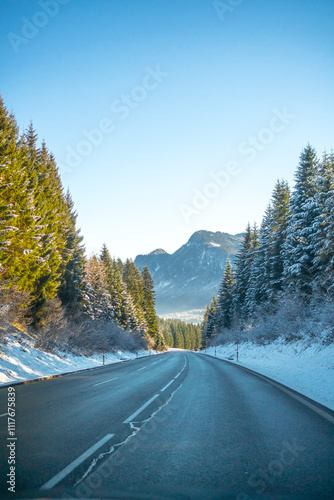 Cars asphalt road between high snowy pine trees. Winter morning in the Alpine mountains region. Concept of traveling by car, transportation, logistics
