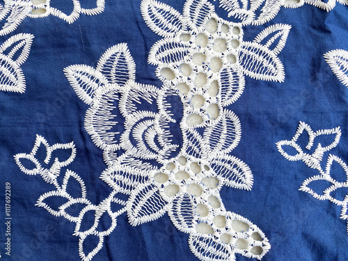 loral design embroidered with delicate white threads, featuring a unique hole design on rich blue cotton fabric.