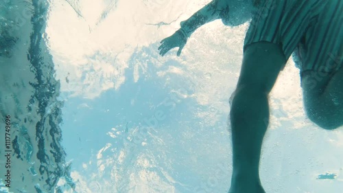 An underwater view from the bottom of the pool of a man falling backwards into the pool wearing a palm tree jacket and shorts making a big splash photo