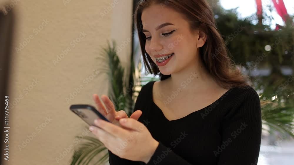 Young woman freelancer uses smartphone, browses internet, chatting, smiles, sits in stylish cafe with laptop. Modern technology, youth lifestyle. Remote studying, e-learning or online remote work Young woman freelancer uses smartphone, browses internet, chatting, smiles, sits in stylish cafe with laptop. Modern technology, youth lifestyle. Remote studying, e-learning or online remote work