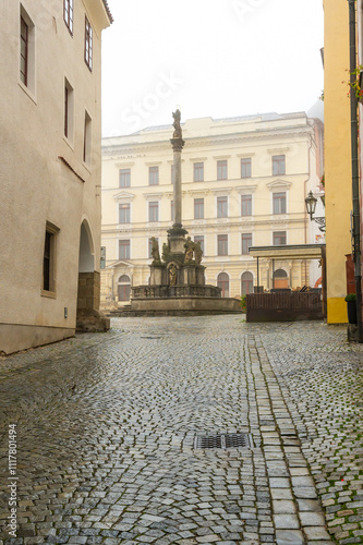 Obraz na płótnie A moody autumn view of the square in Cesky Krumlov, featuring the Baroque Plague Column with the statue of Virgin Mary Immaculata, surrounded by mist, rain, and a tranquil atmosphere w salonie