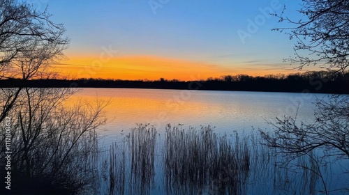 Serene sunset over a tranquil lake, surrounded by silhouettes of trees.