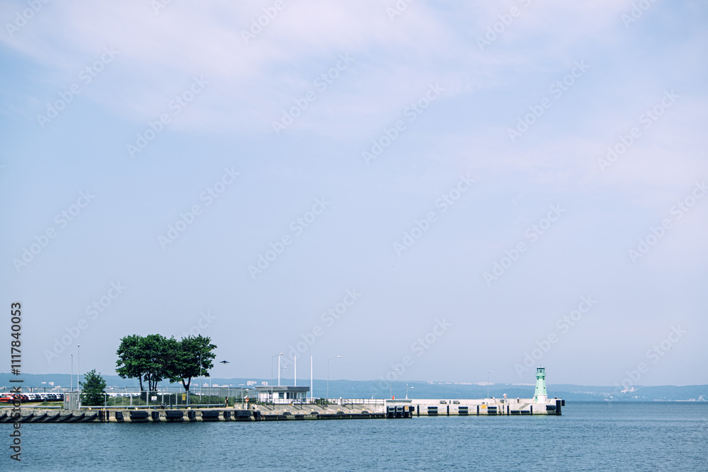 Minimalistic pier with a green lighthouse and trees surrounded by calm waters under a hazy sky. Tranquil coastal scene. Gdansk, Poland - May 19, 2024 Minimalistic pier with a green lighthouse and trees surrounded by calm waters under a hazy sky. Tranquil coastal scene. Gdansk, Poland - May 19, 2024