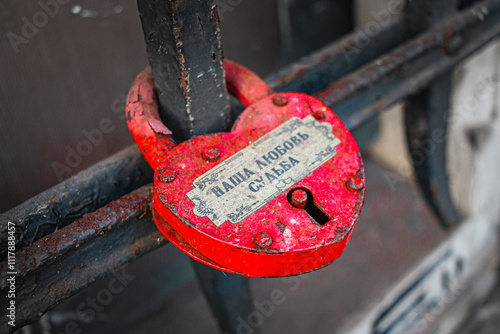 Rustic Red Heart-Shaped Love Lock on Metal Railing Symbolizes Eternal Romance and Commitment with Russian Inscription and Weathered Texture Creating a Nostalgic Atmosphere in an Urban Setting