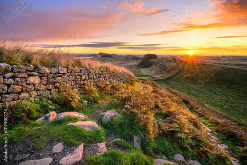 Vibrant summer sunrise at Hadrians Wall overlooking Cuddy's Crags as the sun comes over the horizon. Northumberland, UK.