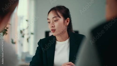 Businesswoman gesturing while speaking during a meeting at a table in an office. Engaging in a discussion, she communicates confidently with an off-screen colleague