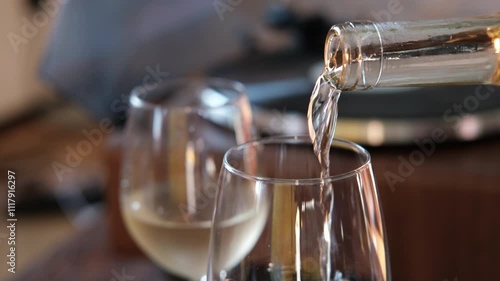 Pouring white wine into a glass from a bottle for cozy aperitif at home on the background of a record player