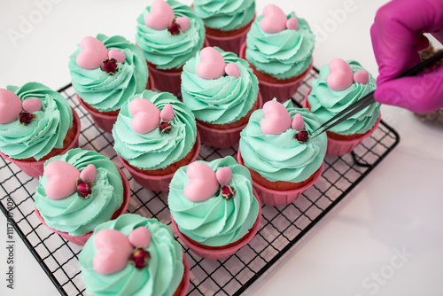Cupcakes. Pink cupcakes with mint cream and pink decoration. Confectioner's hand in a pink glove. Decorate cupcakes