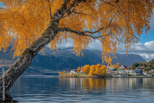 Golden autumn leaves frame a serene view of a village nestled at the foot of majestic Norwegian mountains reflecting in calm waters