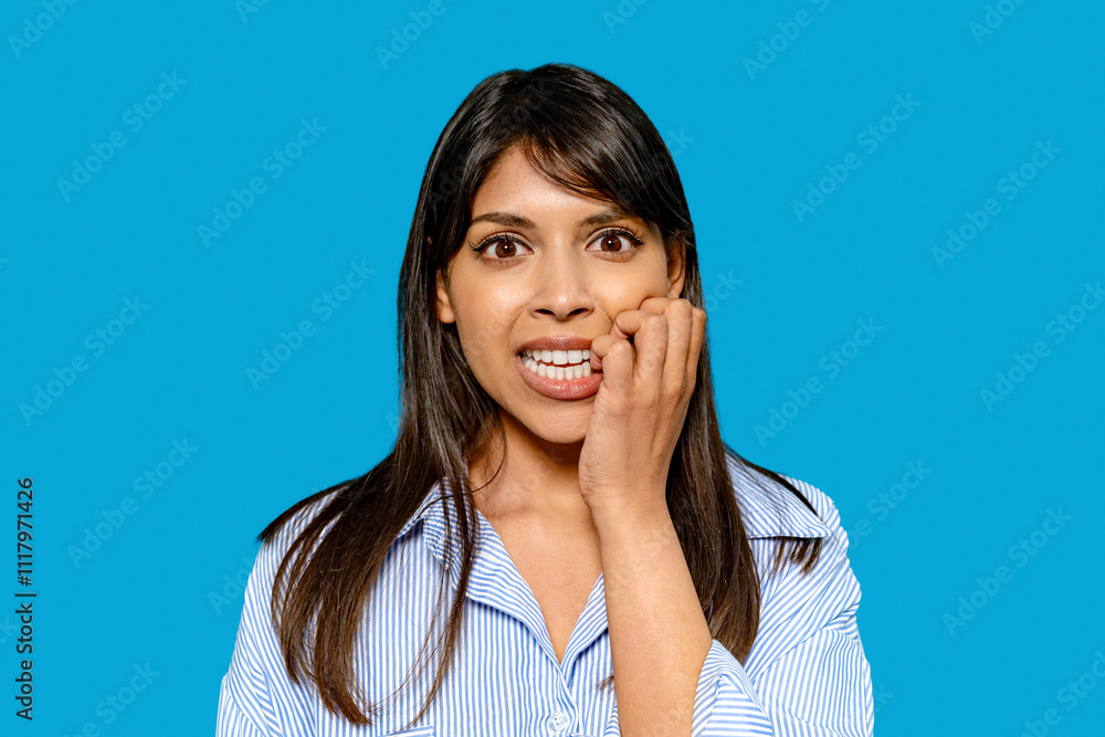 Woman expressing anxiety with a worried look against a bright blue background during an indoor setting Woman expressing anxiety with a worried look against a bright blue background during an indoor setting
