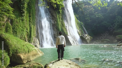 Man backpacker hiking, enjoying waterfall. Travel Lifestyle and Explore Nature concept, vacations into the wild. Hiker travel walking trekking trail in Cikaso Waterfall, Sukabumi, Indonesia. photo