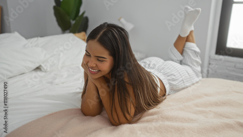 Woman relaxing on a bed looking content in a cozy bedroom, showcasing a serene indoor atmosphere with her brunette hair and attractive smile.