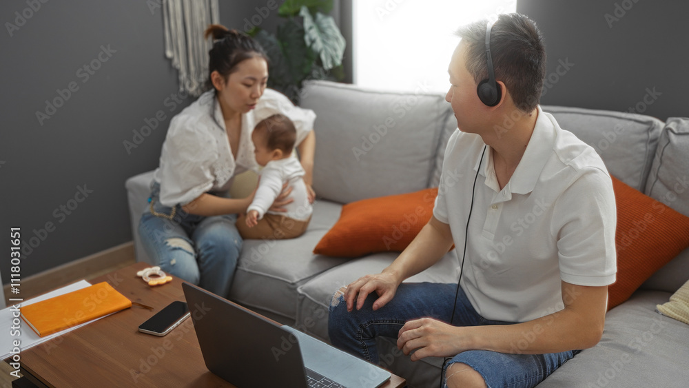 Family spending time together in living room with mother holding baby and father working on laptop, highlighting love in a cozy home environment. Family spending time together in living room with mother holding baby and father working on laptop, highlighting love in a cozy home environment.
