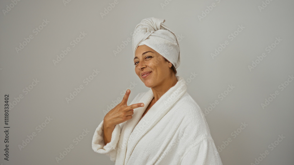 Confident, mature, hispanic woman in a bathrobe and towel on her head, giving a peace sign while standing isolated against a white background, emanating beauty and relaxation. Confident, mature, hispanic woman in a bathrobe and towel on her head, giving a peace sign while standing isolated against a white background, emanating beauty and relaxation.