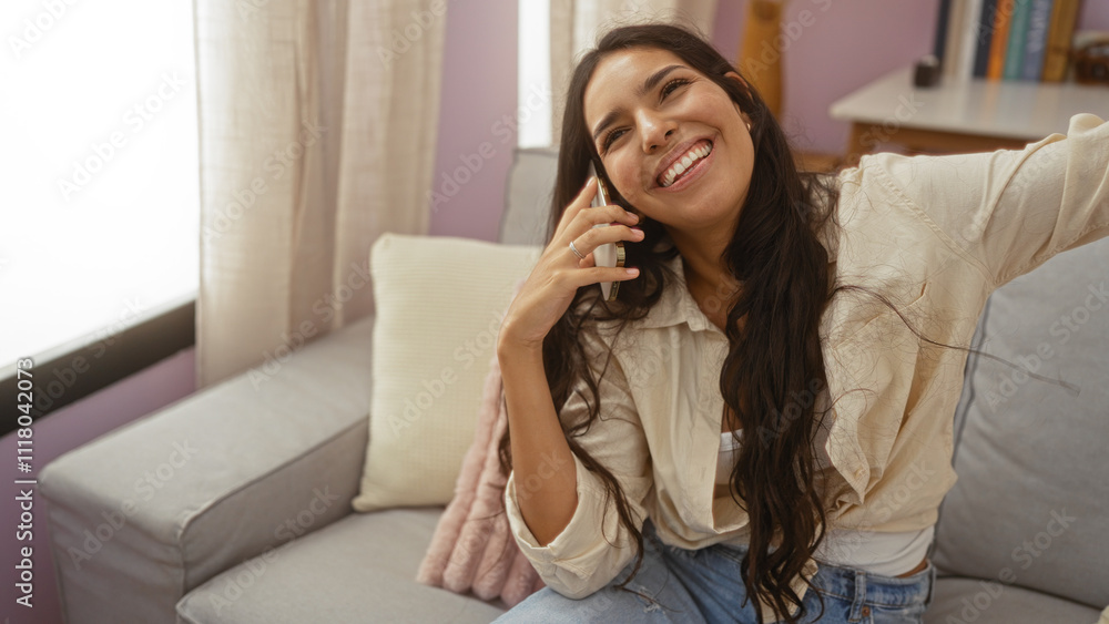 Young woman with long brunette hair talking on the phone while sitting on a sofa in a cozy living room with soft lighting Young woman with long brunette hair talking on the phone while sitting on a sofa in a cozy living room with soft lighting