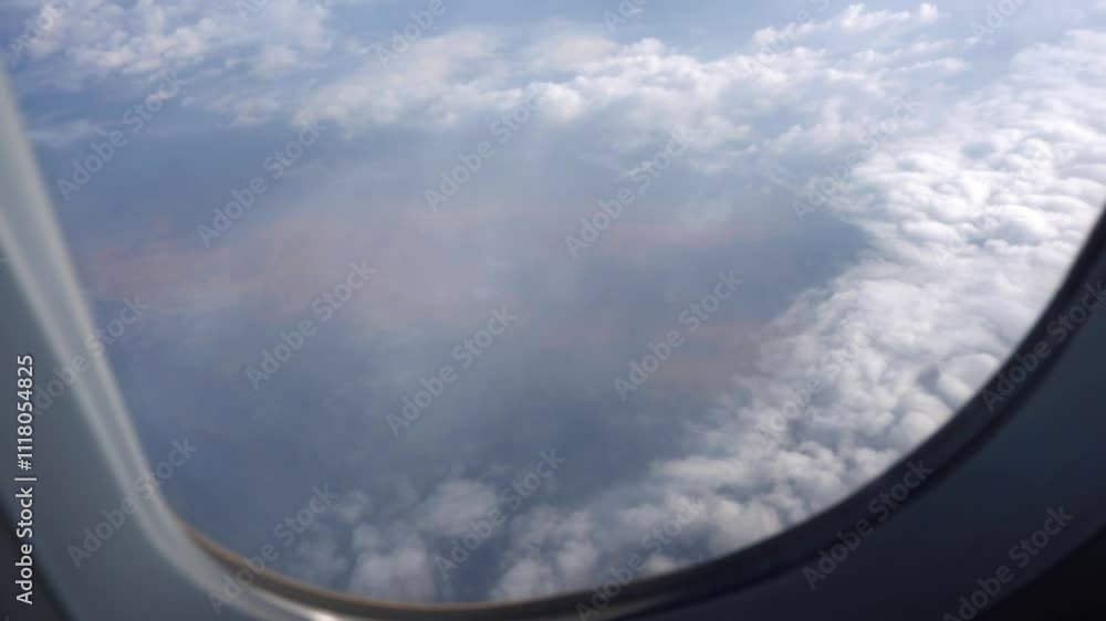The view from the plane window of the white clouds. The silver wing of an airplane. Brown earth is visible in places. Shadows from clouds fall on neighboring clouds. The window of the plane. The view from the plane window of the white clouds. The silver wing of an airplane. Brown earth is visible in places. Shadows from clouds fall on neighboring clouds. The window of the plane.