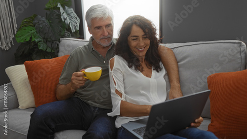 Couple smiling together on sofa with laptop and coffee, creating a cozy home atmosphere in living room.