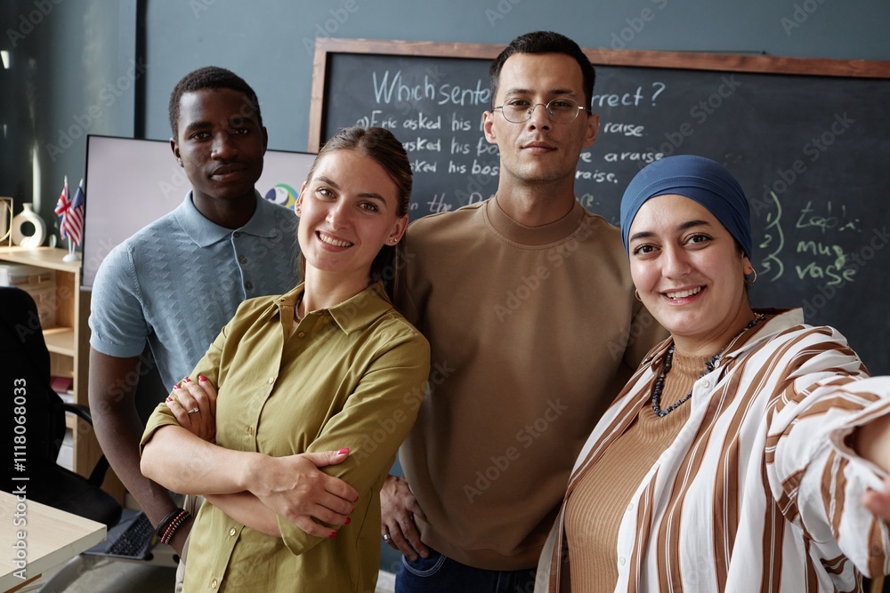 Obraz premium Smiling Muslim woman snapping selfie with diverse team of English teachers posing against blackboard in classroom of language school