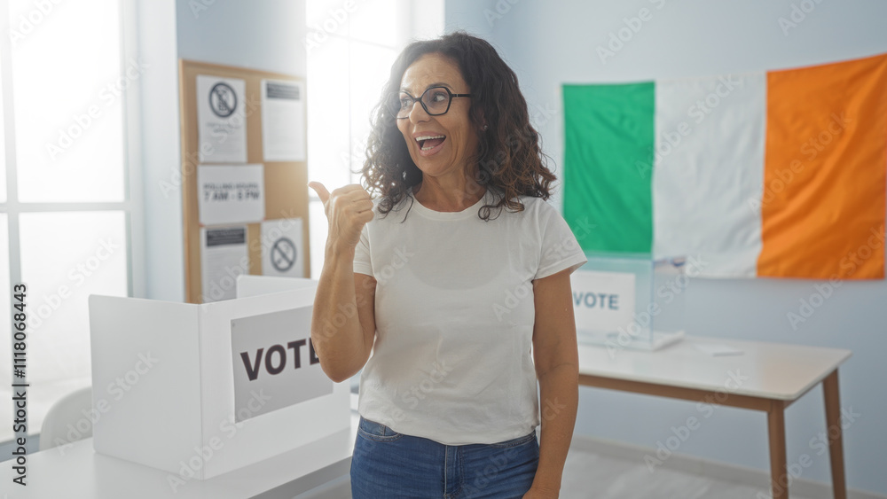 Woman pointing with her thumb inside an electoral room at an irish voting site with a flag and voting booth nearby Woman pointing with her thumb inside an electoral room at an irish voting site with a flag and voting booth nearby