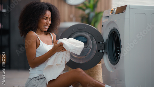 African American female woman girl ethnic lady housewife homeowner housework at floor open washing machine smell clean white towel cloth bad smelling sniff terrible aroma laundry conditioner gel stink