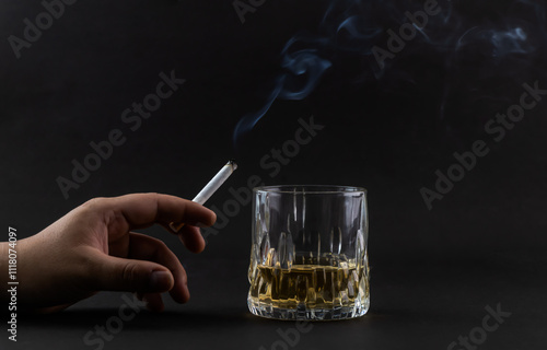 A burning cigarette in one hand and a glass of alcohol on the black background.