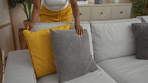 Bilde på lerret Woman arranging yellow and gray pillows on a modern gray sofa in a cozy, home in