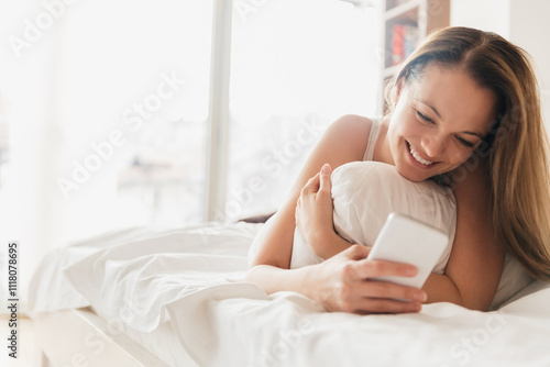 Smiling woman in bed using smartphone