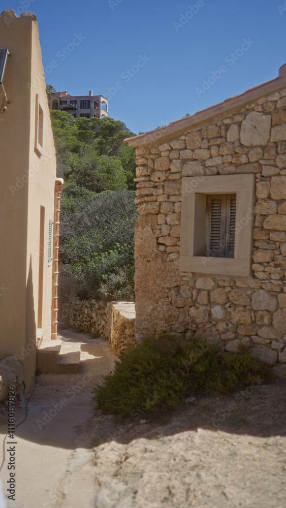 Naklejka premium Rustic stone path between traditional houses in mallorca with a scenic view of the countryside on a sunny day.