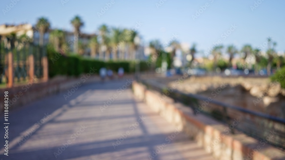 Blurred image of people walking on a paved path with lush greenery and palm trees in the background with a bright sunny sky Blurred image of people walking on a paved path with lush greenery and palm trees in the background with a bright sunny sky