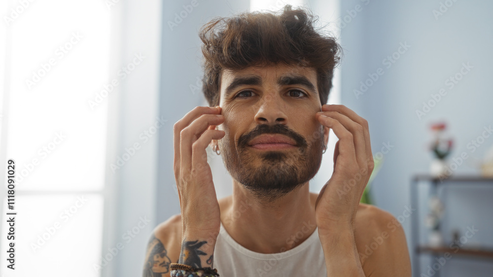 Handsome young man with a beard in a spa room, touching his face in a wellness center, highlighting his tattoos and relaxed expression. Handsome young man with a beard in a spa room, touching his face in a wellness center, highlighting his tattoos and relaxed expression.