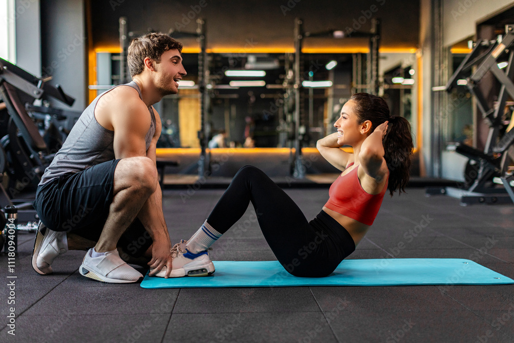 Fit young woman exercising with male personal trainer in gym on mat, doing abs workout in fitness gym, side view Fit young woman exercising with male personal trainer in gym on mat, doing abs workout in fitness gym, side view