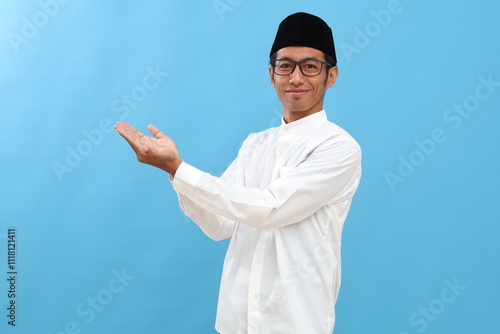 Young asian man wearing typical muslim clothes isolated on blue background holding a copy space on a palm. photo