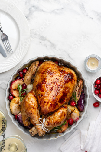 Roasted chicken with apples, red onions and cranberries in a ceramic form. Christmas dish.  Marble background. Top view. Copy space