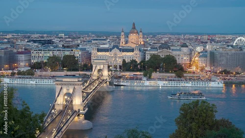 Beautiful view of the Chain Bridge and St. Stephen's Basilica in Budapest, Hungary, at dusk, with street lights glowing and boats gently drifting on the Danube River