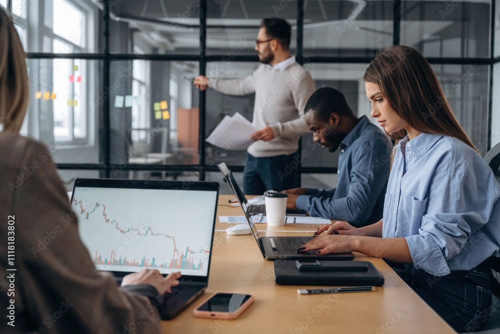 Man is standing by the glass, showing information. Professional workers are in the modern office together Man is standing by the glass, showing information. Professional workers are in the modern office together
