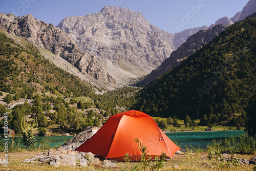 A tourist tent stands by a mountain lake against a background of rocks and peaks. Camping in the mountains in summer photo