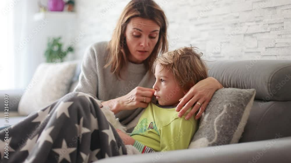 Sick child, preschool boy, lying in bed with a fever, resting at home with his pet dog, mom checking on him Sick child, preschool boy, lying in bed with a fever, resting at home with his pet dog, mom checking on him