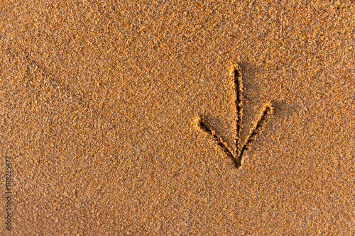 Directional arrow written on sand near ocean. Close up of arrow sign pointing down photo