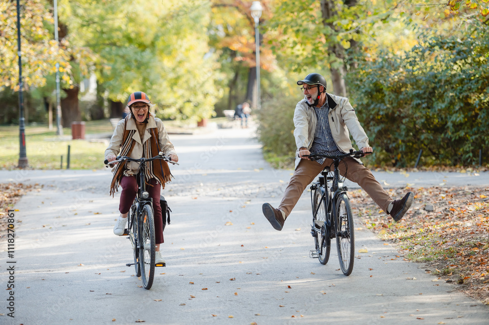 Fototapeta premium Senior couple riding bicycles together through an autumn park, laughing and enjoying an active lifestyle, showcasing fun, health, and companionship in a vibrant outdoor setting