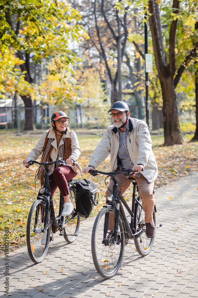 Fototapeta premium Senior couple riding bicycles together through an autumn park, laughing and enjoying an active lifestyle, showcasing fun, health, and companionship in a vibrant outdoor setting